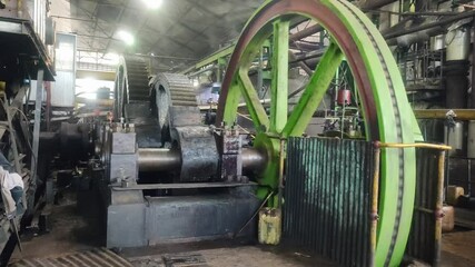 Vintage steam engine powering sugarcane crusher at sugar mill. Historical industrial machine showing traditional process of juice extraction from sugarcane stalks.