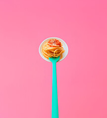 Concept of Italian food with delicious paste, spaghetti with tomato souse on turquoise green fork on pink background.