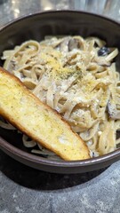 Fresh tagliatelle pasta with creamy truffle sauce and garlic bread in dish at Italian restaurant 