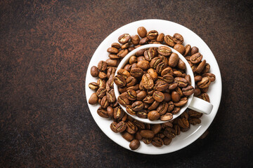 Roasted coffee beans in white cup at dark table.