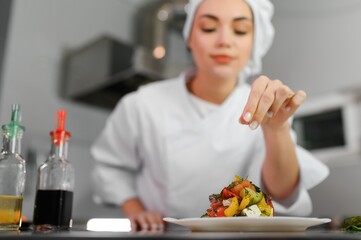 Female Chef in hotel or restaurant kitchen cooking, she is finishing a dish on plate