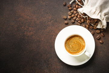 Cup of coffee, roasted coffee beans and filter holder at dark table.