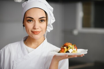 Female Chef in hotel or restaurant kitchen cooking, she is finishing a dish on plate