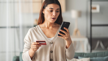 Woman holding credit card and mobile phone in her hand in shock