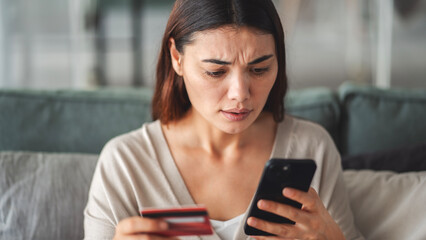 Woman holding credit card and mobile phone in her hand in shock