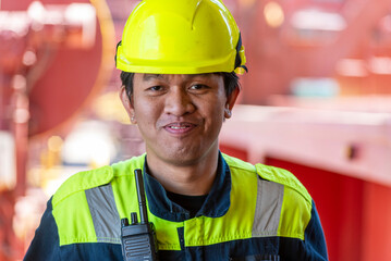 Portrait of a young Filipino officer in protective clothing and a yellow helmet, standing aboard a container ship—his eyes focused ahead, reflecting both duty and quiet determination.