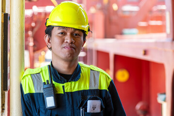 Portrait of a young Filipino officer in protective clothing and a yellow helmet, standing aboard a container ship—his eyes focused ahead, reflecting both duty and quiet determination.