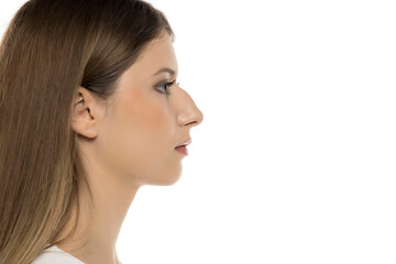 Naklejka premium This image features a side profile of a young woman with long brown hair, showcasing her delicate features and calm expression against a clean white background.