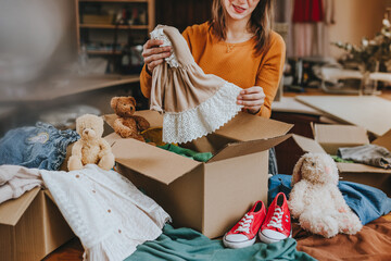 Woman sorting an old out-of-use kid toy, clothes and shoes in box for charity or upcycling