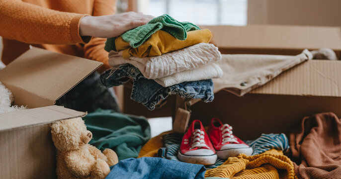 Woman sorting an old out-of-use kid toy, clothes and shoes in box for charity or upcycling