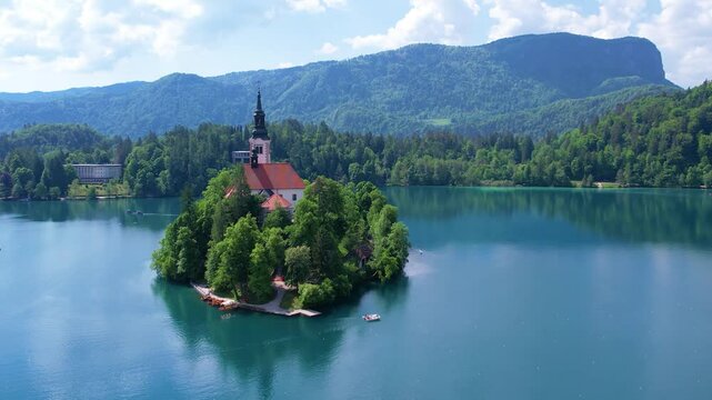 Aerial view of Church of the Assumption of Mary in the center of the lake Bled. Flying around small island on Bled Lake in Slovenia, warm summer day sun