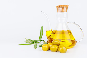 Still life of olive oil cruet, green olives, and olive branches on white table