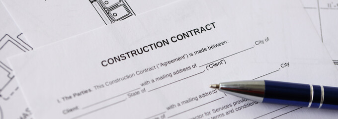 Pen on residential construction agreement and planning blueprints of residential building project...