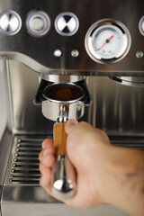 A close-up view of a hand inserting a portafilter filled with ground coffee into a modern espresso machine. Stainless steel finish, pressure gauge visible—perfect for coffee brewing, barista training,