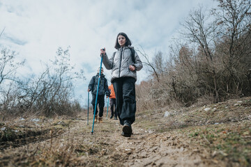 Outdoor enthusiasts hiking together on a natural trail with hiking poles, set against a serene autumn backdrop of a dried and barren landscape under a cloudy sky.
