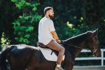 A man is peacefully riding a horse in an outdoor setting, surrounded by lush greenery, capturing a...