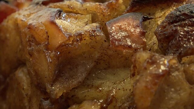 Extreme close-up of a baked apple and bread dessert with visible caramelization, glistening syrup, and cinnamon coating.
