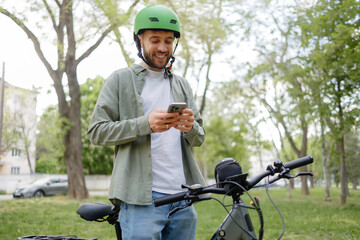 Fototapeta premium Young man enjoys park time on bicycle while using smartphone to connect with friends outdoors