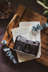 Retro camera on old book and eucalyptus branch on wooden background, flat lay. Vintage style