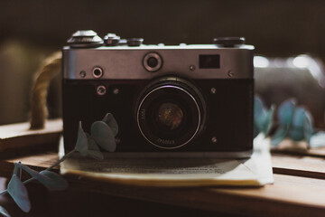 Retro camera on old book and eucalyptus branch on wooden background. Vintage style