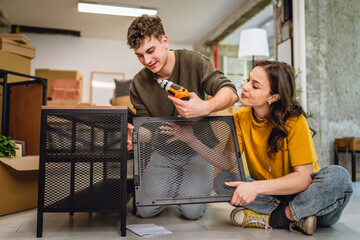 Adult couple use electric drill for assembling table at new apartment