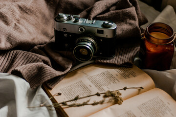 Vintage film camera with an old book wrapped in a warm knitted sweater and an extinguished candle next to it. View from above on a flat surface.