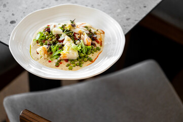 gourmet dish with shrimp, peas, and mixed greens on a creamy sauce, elegantly plated on a white dish. Vibrant colors and fresh ingredients create a visually appealing and appetizing meal