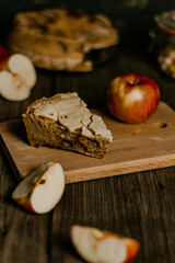 Traditional apple pie Charlotte apples are lying nearby. Sweet Thanksgiving dinner, autumn seasonal apple pie sliced one piece on wooden tray, on dark wooden background.