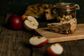 Traditional apple pie Charlotte apples are lying nearby. Sweet Thanksgiving dinner, autumn seasonal apple pie sliced one piece on wooden tray, on dark wooden background.