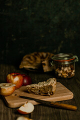 Traditional apple pie Charlotte apples are lying nearby. Sweet Thanksgiving dinner, autumn seasonal apple pie sliced one piece on wooden tray, on dark wooden background.