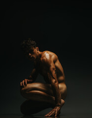 Fototapeta premium A muscular man kneels in a dynamic pose, captured under low-light dramatic shadows.