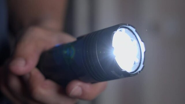 Close-up of a hand holding a flashlight, switching it on and casting light on an interior wall. Useful scene for emergencies, power outages, or nighttime searching
