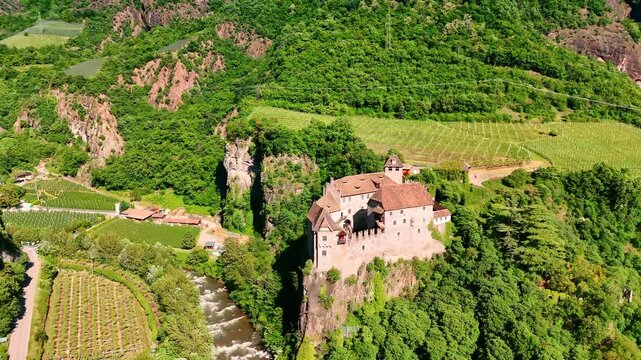 Medieval fortification of Runkelstein Castle on the spur of the rock. River flows at the foot and vast vineyards grow around. Bolzano, South Tyrol, Italy. Aerial view.