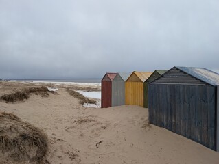 A vibrant and vivid row of colorful beach huts stands proudly on a sunkissed sandy beach, creating a picturesque seaside view
