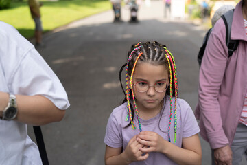 Sad girl with colorful dreadlocks on a path in the park in summer. Concept of children's emotions