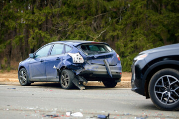 Blue compact car with severe rear end damage after highway collision, debris scattered on the road...