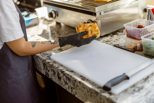 A skilled chef wearing gloves carefully prepares an appetizing and delicious sandwich in a modern kitchen setting