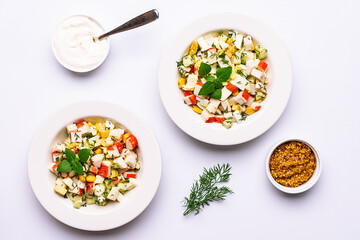 Fresh crab stick salad with cucumber, dill, eggs, corn and homemade mayonnaise sauce on light table top view.
