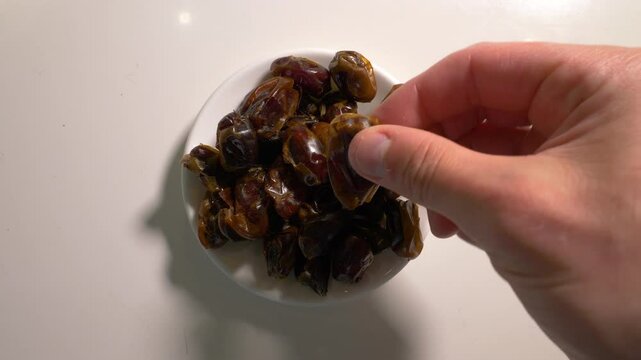 Man puts dried dates fruits in a plate on the kitchen table. Slow motion. Top view.
