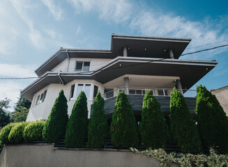 A contemporary multi-story house with a distinctive design, featuring manicured greenery and a...