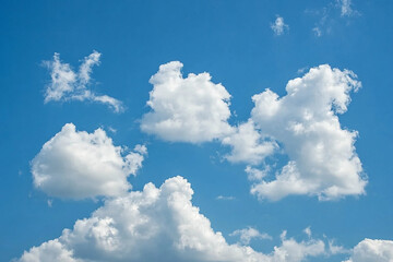 Daytime sky with fluffy white cumulus clouds scattered across a clear blue sky