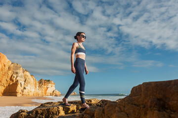 sporty woman walking across rocks at the coast in the sun