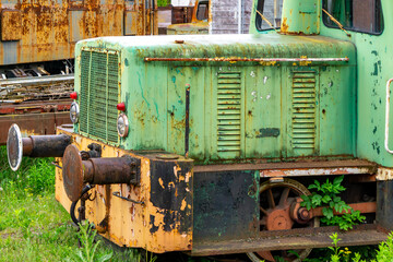 Close-up of a rusty green and yellow shunting locomotive standing on an overgrown railway track....