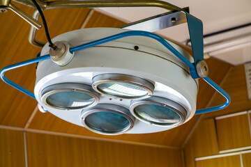 Close-up of a vintage surgical lamp with four blue lenses, mounted on the ceiling of an old operating room. This retro medical equipment, typical of hospitals from the 1960s and 1970s, highlights the 