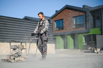 Male Worker using vibratory plate compactor to firm soil at worksite. builder. After laying of...