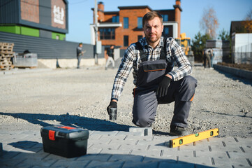 Construction worker installing and laying pavement stones on terrace, road or sidewalk. Worker...