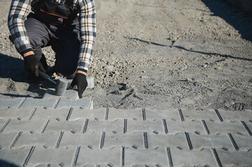 Builder laying a paving brick placing it on the sand foundation with gloved hands