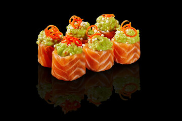 Salmon uramaki sushi rolls topped with guacamole and chili pepper reflecting on black background