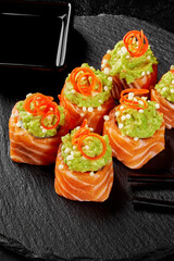Delicious uramaki sushi rolls with salmon, avocado, masago and carrot on black slate