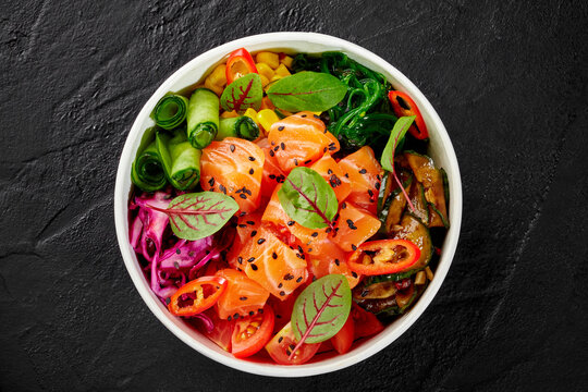 Salmon poke bowl with cucumbers, corn, red cabbage, tomatoes, wakame seaweed, sesame seeds and chili pepper